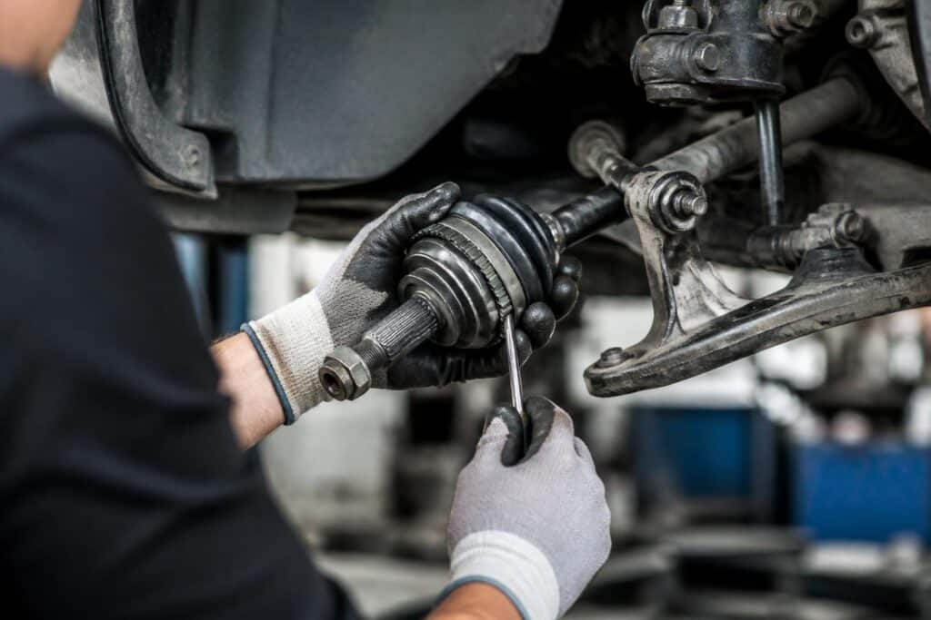 Mãos de um mecânico consertando a homocinética de um carro em uma oficina automotiva.