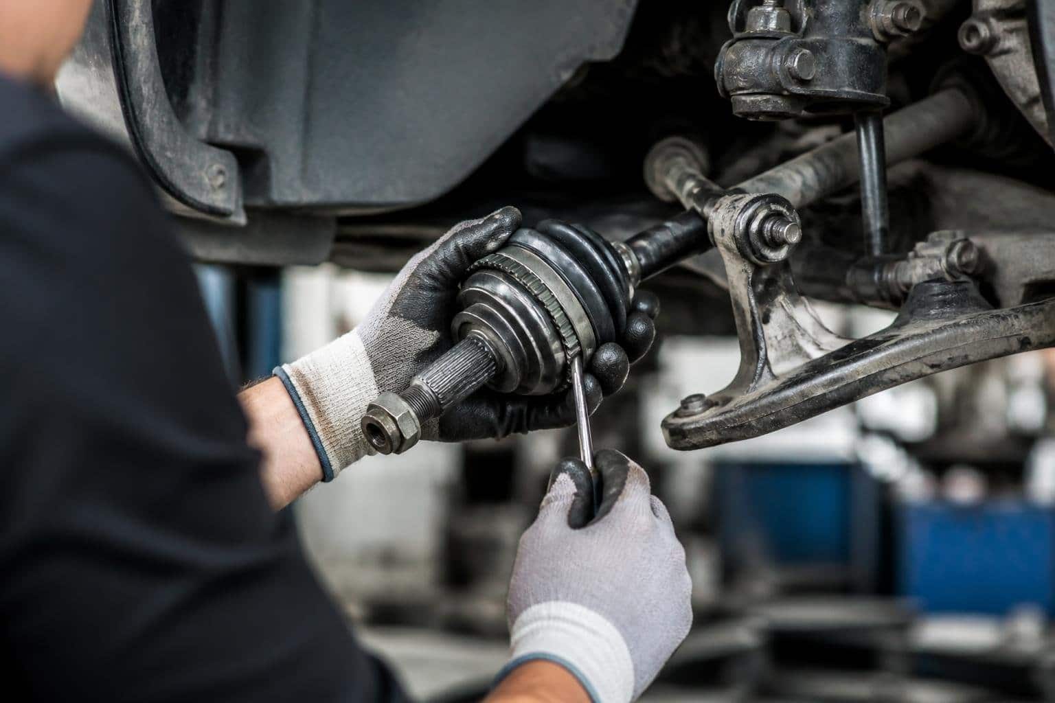 Mãos de um mecânico consertando a homocinética de um carro em uma oficina automotiva.